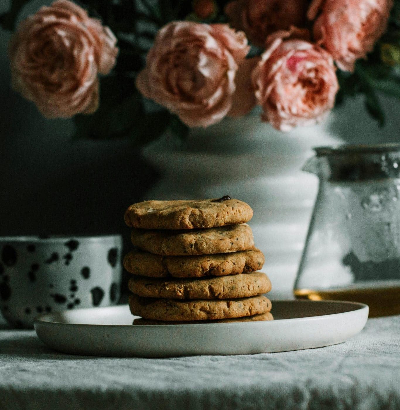 A plate of cookies stacked up on a blue table cloth with flowers behind