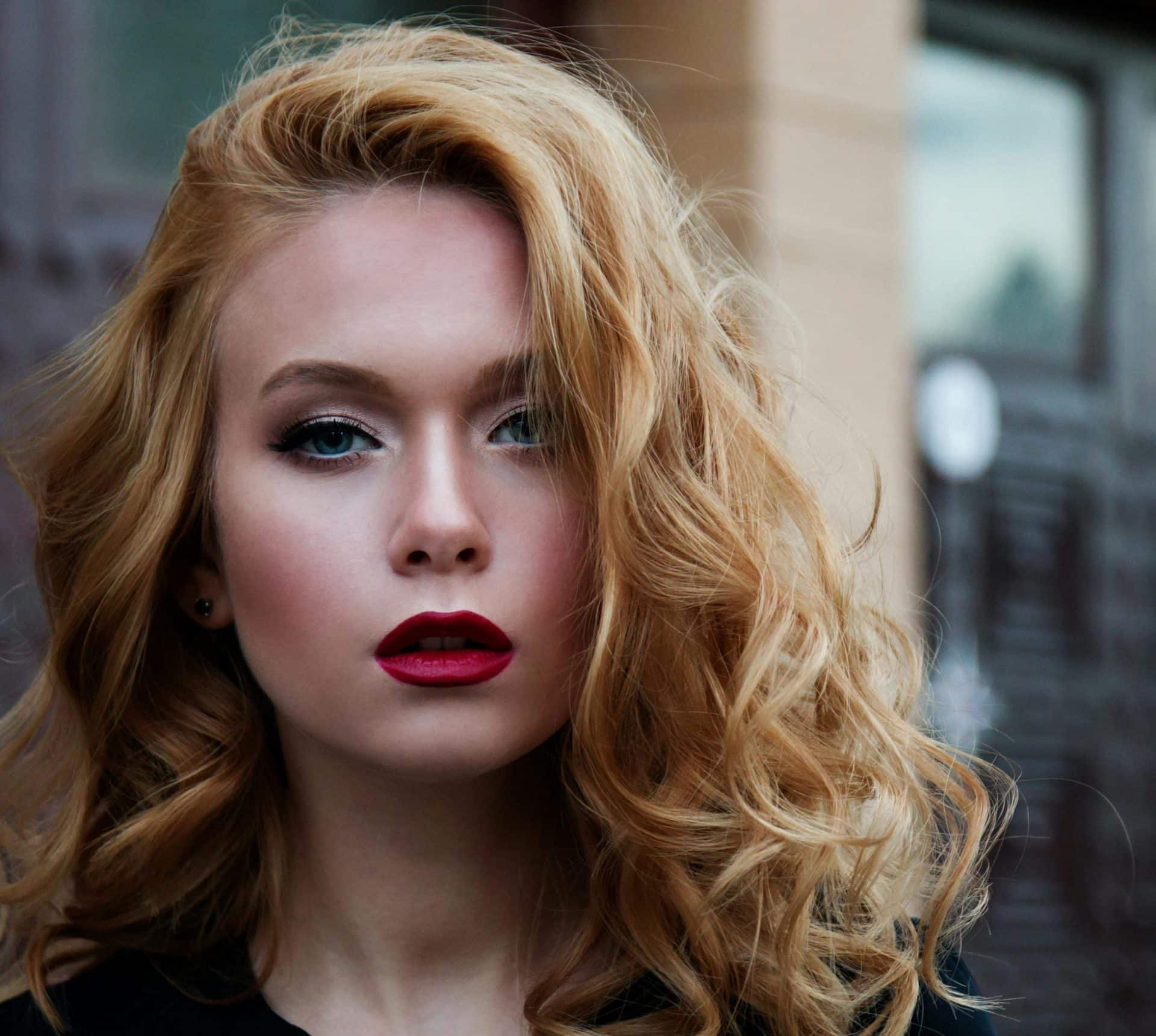A woman's face with auburn curly hair and bright red lip stick